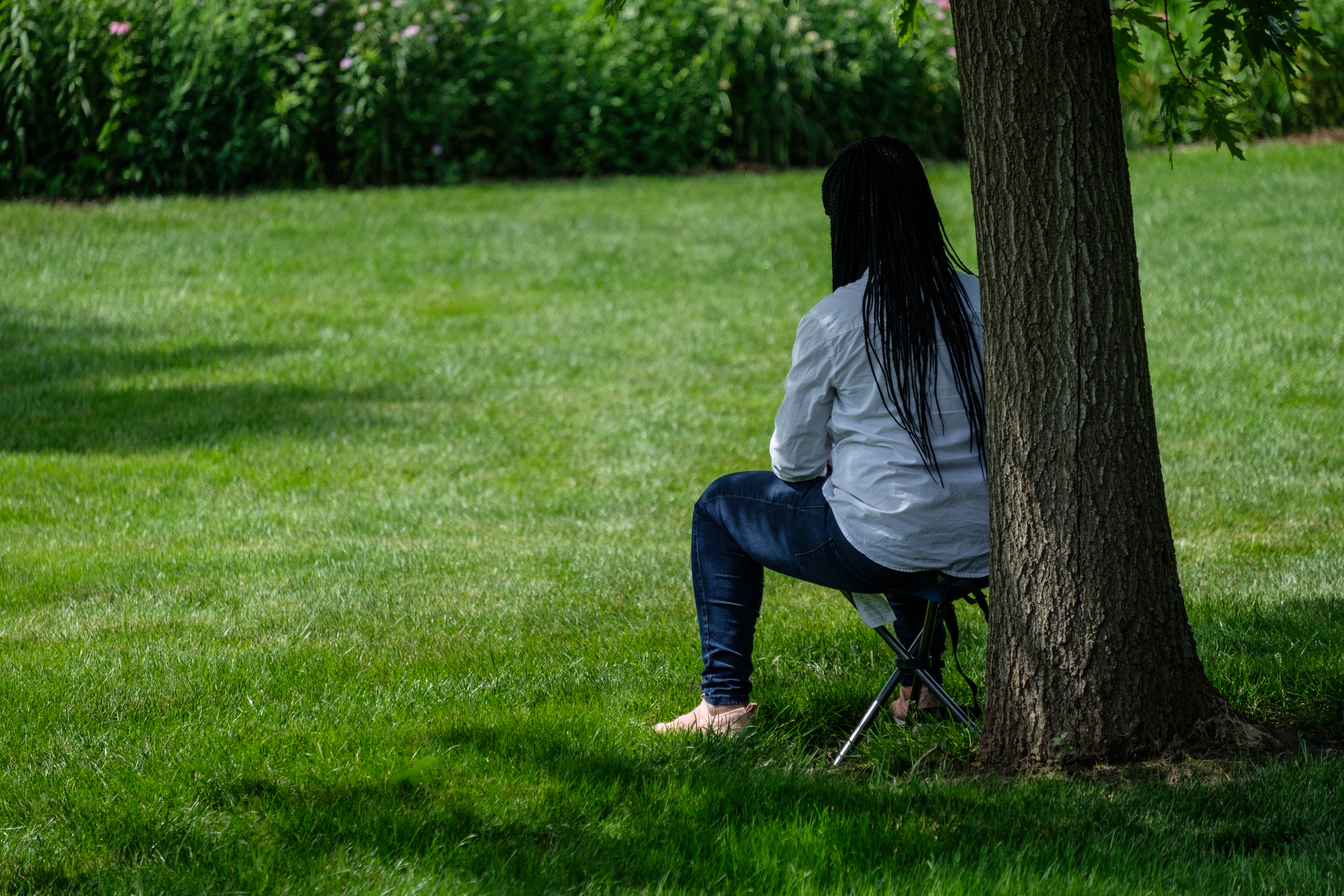 A teacher sits under a tree, facing away form the camera.